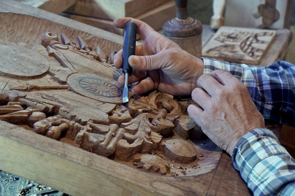 Holzschnitzerei. Schnitzer mit Meißel. Ein geschickter Handwerker arbeitet an einer Holzschnitzerei-Dekoration - Foto, Bild