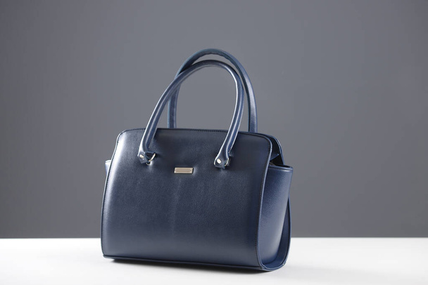 Modern fashionable women handbag. Elegant reptile leather blue women bag on white table and gray background - Photo, Image