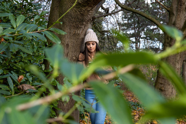 Nuori nainen talvella yllään villapaita ja vaaleanpunainen bobble hattu metsässä puistossa joku katselee ja vakoilee niitä oksien ja pensaiden läpi, tirkistely vaanii käsite. - Valokuva, kuva