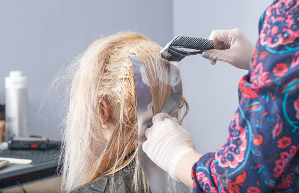 Coloration des cheveux d'un ton clair, une jeune femme européenne teint ses cheveux dans un salon, travail de coiffeur, salon de beauté. - Photo, image