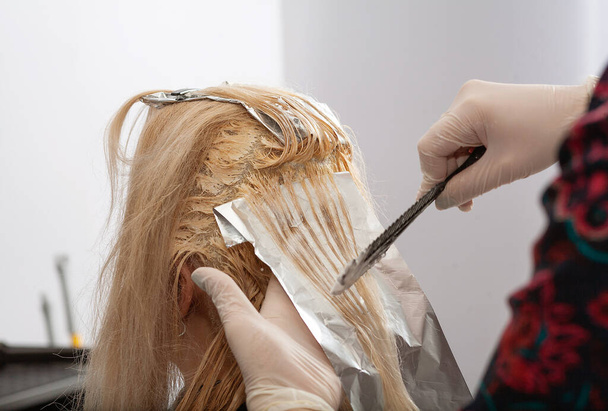 Haarfärbung in einem hellen Ton, eine junge Europäerin färbt ihre Haare in einem Salon, Friseurarbeiten, Schönheitssalon. - Foto, Bild