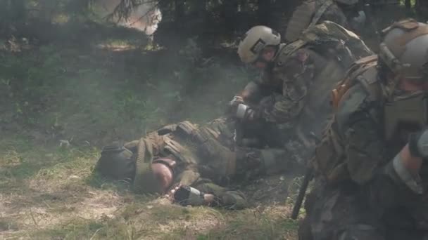 Imágenes de soldados que ayudan a un compañero herido tendido en el suelo, aplicándose torniquete en la pierna y defendiéndose de los enemigos - Metraje, vídeo