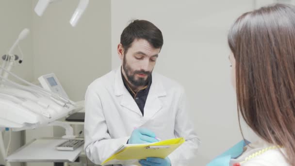 Baard tandarts vullen van medische documenten tijdens het praten met de patiënt - Video
