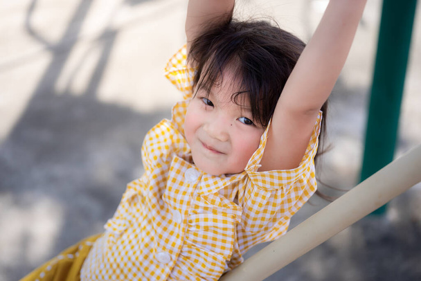 Aktív gyerek trapézt játszik a játszótéren. Gyönyörű gyerek, édes mosollyal a kamerába néz. A boldog gyerekek sárga inget viselnek. 5-6 éves csecsemő. - Fotó, kép