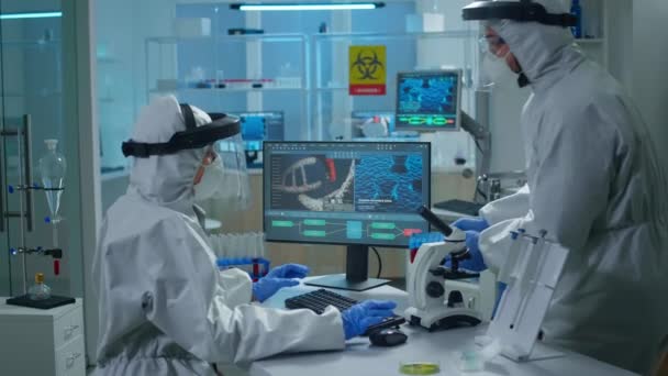 Χημικός με στολή ppe εργάζεται στο PC ενώ τεχνικός εργαστηρίου φέρνοντας δείγματα αίματος της - Πλάνα, βίντεο