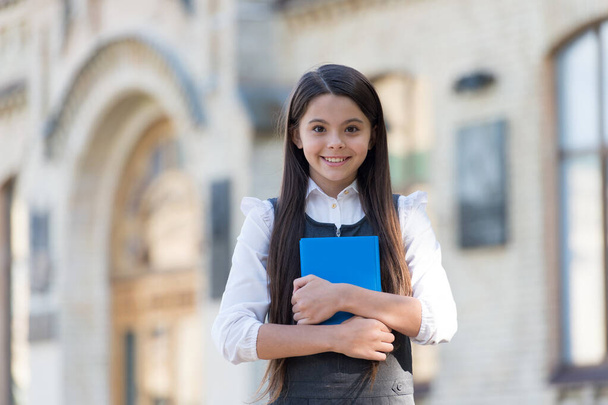 Happy small kid with school look wear uniform holding library book outdoors, knowledge - Valokuva, kuva