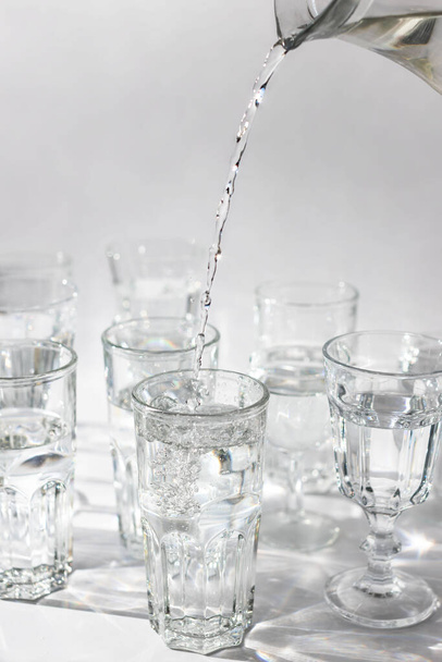 Hand pours fresh water from a decanter into a glass, light background. Close up, vertical.	 - Valokuva, kuva