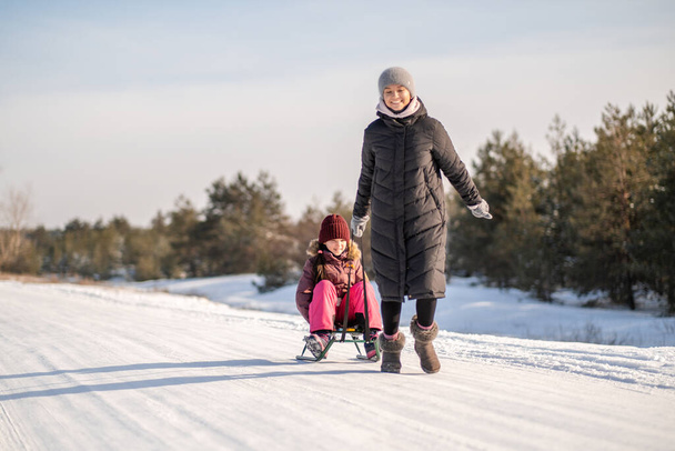 Diversión familiar de invierno en el parque. Madre e hija se divierten al aire libre en la nieve en invierno. - Foto, Imagen