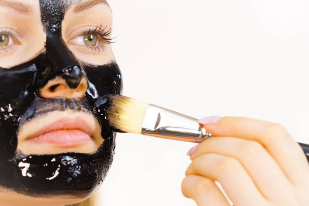 顔にブラシブラックのデトックスピールマスクで適用若い女性。女の子は肌の世話をする。美の治療だ。スキンケア. - 写真・画像