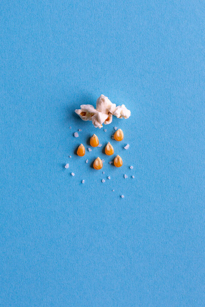 Petit nuage de maïs soufflé avec pluie faite de grains de maïs et de sel sur fond bleu avec espace de copie - Photo, image