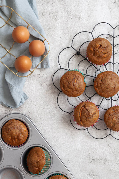 Colocação plana de muffins recém-assados em um rack de resfriamento preto com ovos em uma cesta e uma bandeja de cozimento com muffins - Foto, Imagem