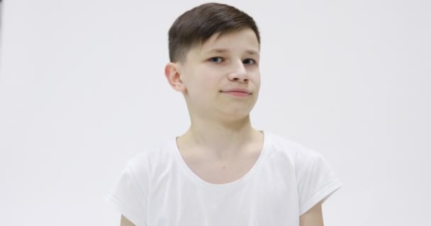 Όμορφος έφηβος 14s σε λευκό t-shirt ευτυχώς χαμογελαστός απομονωμένος πάνω από λευκό φόντο στο στούντιο. Άνθρωποι ειλικρινή συναισθήματα, έννοια του τρόπου ζωής. Κοιτάζοντας την κάμερα με γοητευτικό χαμόγελο, έκπληξη. - Πλάνα, βίντεο