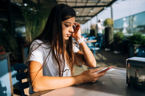 Jovem mulher em um café segurando um smartphone em suas mãos - Foto, Imagem