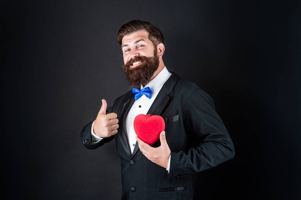 happy tuxedo man with beard hold romantic love heart show thumb up, happy valentines day - Fotografie, Obrázek