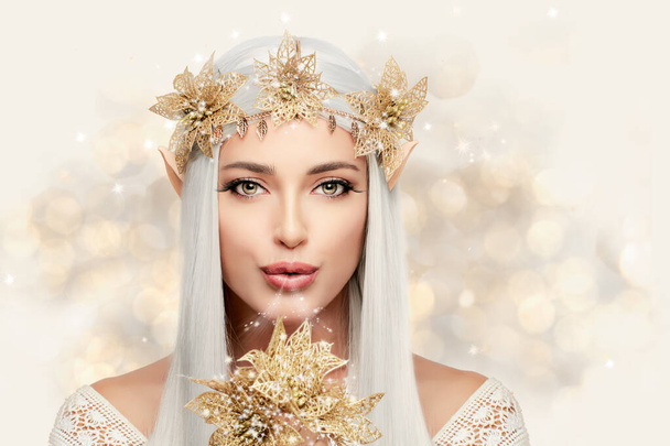 Attractive elf queen with golden flowers looking at camera while standing against shimmering lights. Beautiful young woman with fairy tale costume - Photo, Image