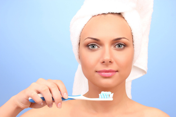 Beautiful young woman after shower with a towel on her head and a toothbrush in hand on a blue background close-up  - Fotoğraf, Görsel