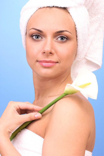 Beautiful young woman after shower with a towel on her head and white calla on blue background close-up - Foto, immagini