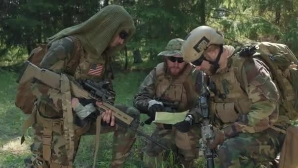 Mittlere Aufnahme von vermummten Pfadfindern mit schwarzer Sonnenbrille bei der Untersuchung der Karte des Militäreinsatzes im Dschungel - Filmmaterial, Video