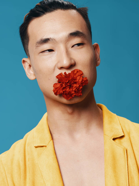 Happy male of Korean appearance on a blue background with a flower in his mouth - Foto, immagini