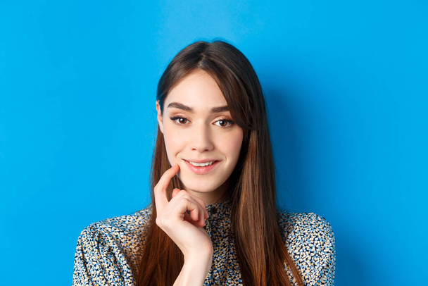 People emotions concept. Close-up portrait of intrigued pretty lady smiling and looking thoughtful, being interested, standing on blue background - Foto, Bild