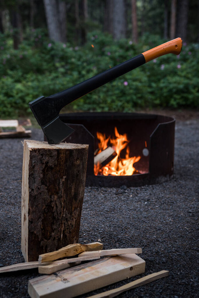Splitting firewood with a chopping axe for burning a fire at a campsite. Warm fiery glow in firepit in the evening. Logs and wood kindling - Φωτογραφία, εικόνα