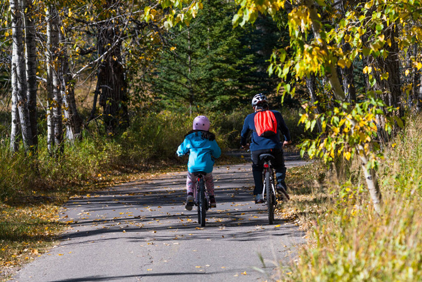 Батьки та діти їздять на велосипедах у парку. Батько і дочка катаються на велосипеді в осінні довгі вихідні. Сімейна активність та веселий спосіб життя
 - Фото, зображення