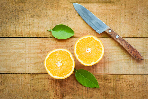 Свіжий апельсиновий шматочок і листя здорових фруктів, апельсинові фрукти з листям кухонного ножа на дерев'яному фоні вид зверху
  - Фото, зображення