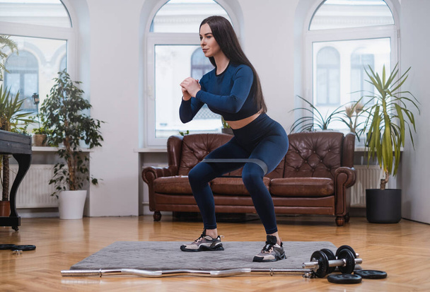 Geconcentreerde vrouw doet yoga met weerstandsband in appartement - Foto, afbeelding