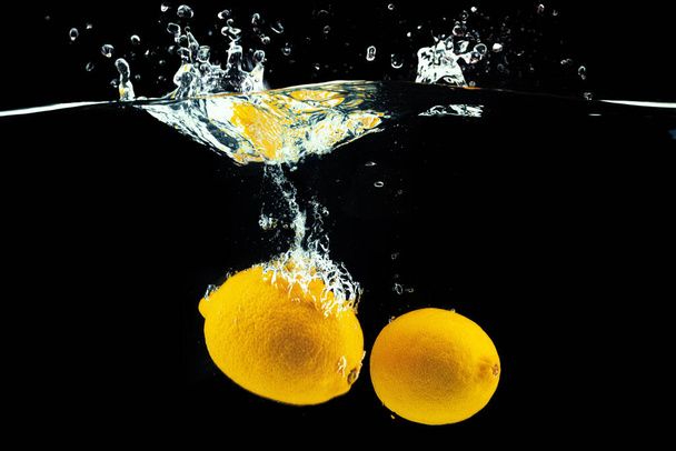 Lemons diving into the water with a splash against black background - Foto, Imagem