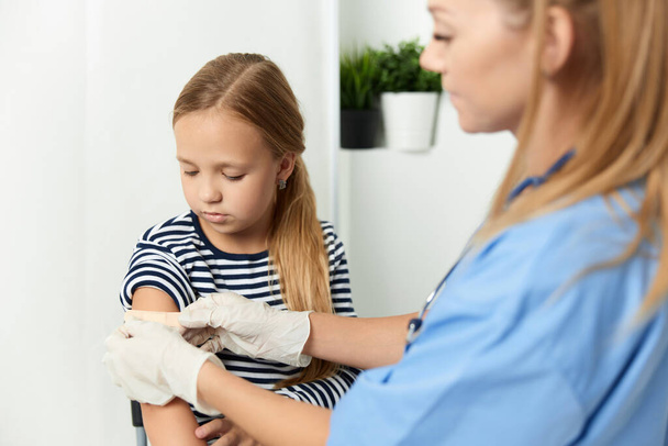 a woman doctor next to a girl seals her hand with a health adhesive - Fotografie, Obrázek