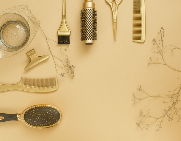 The background is beige with hairdressing tools and dried flowers. Gold hair accessories, template with copy space. - Foto, Imagem