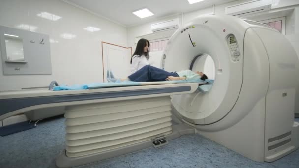 Жіночий пацієнт проходить КТ або МРТ сканування під наглядом радіолога в сучасній медичній клініці. Пацієнт лежить на КТ або МРТ сканування ліжка, рухаючись за межі машини. - Кадри, відео