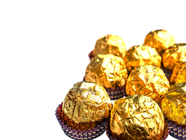Chocolates redondos en una envoltura de lámina dorada sobre un fondo blanco. - Foto, Imagen