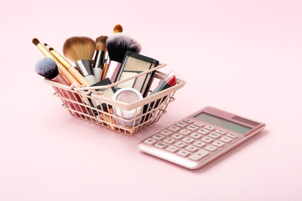 Maquiagem produtos de beleza na cesta de compras com calculadora em fundo rosa pastel - Foto, Imagem