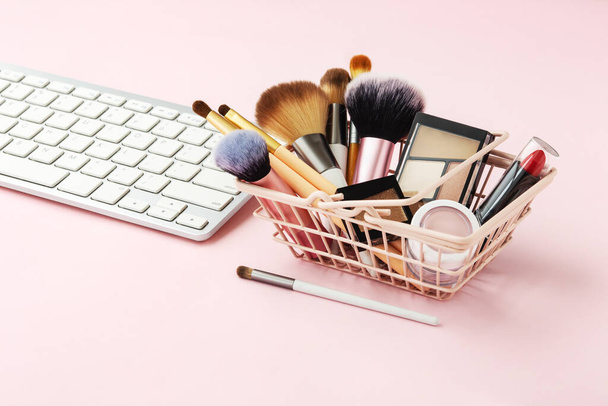 Makyaj ve kozmetik online alışveriş, alışveriş sepeti ve bilgisayar klavyesi ve pastel pembe masa üzerinde ürünler. - Fotoğraf, Görsel
