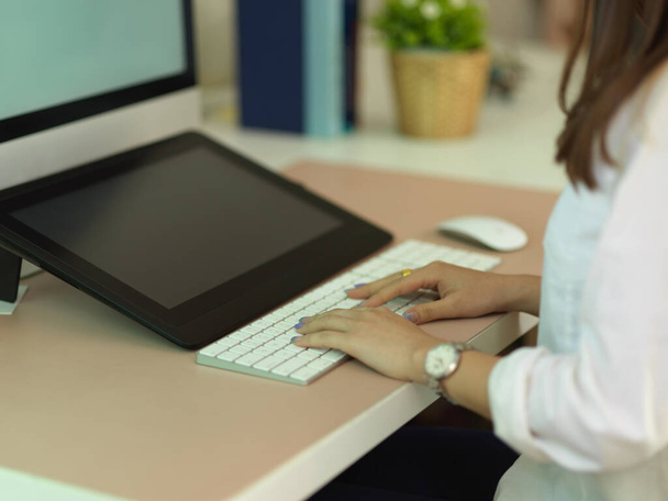 Side view of female office worker hand typing on computer keyboard on worktable in office room - Fotó, kép