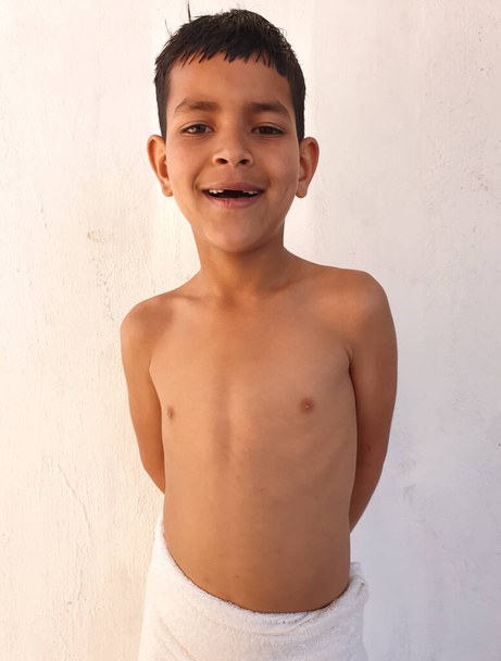 Portret indyjskiego chłopca uśmiechającego się ze złamanymi zębami, małego chłopca w białym ręczniku, azjatyckiego dzieciaka patrzącego w kamerę - Zdjęcie, obraz