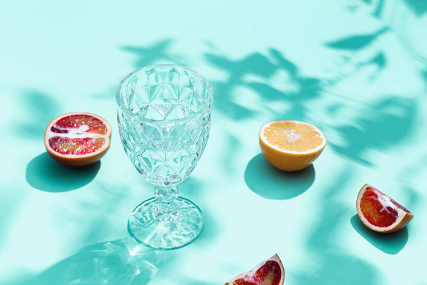 Bright slices citrus fruits and glass with water on pastel turquoise colored background. Fruit food and summer concept. - Фото, зображення