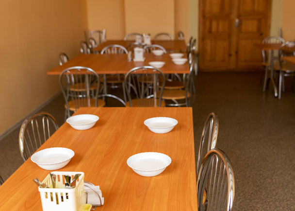 immagine con tavoli e sedie nella sala da pranzo della scuola, ciotole bianche con pranzo sul tavolo - Foto, immagini