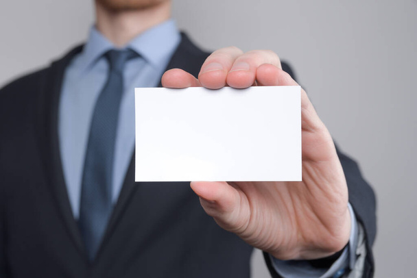 ビジネスマン、ビジネスマンの手の中に名刺を示す-灰色の背景で撮影を閉じます。空白の紙を見せてください。紙訪問カード. - 写真・画像