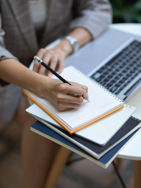 Vágott felvétel női kézírás üres notebook, miközben dolgozik laptop dohányzóasztalon - Fotó, kép