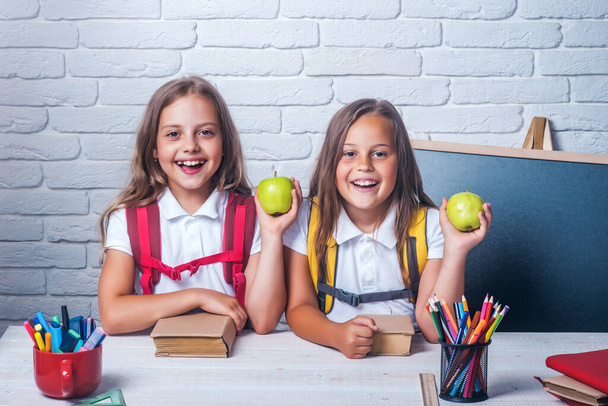 Back to school and home schooling. Friendship of small sisters in classroom at knowledge day. Little girls eat apple at lunch break. School time of girls. Happy school kids at lesson. - Φωτογραφία, εικόνα