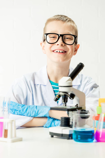 Un écolier avec un microscope examine les produits chimiques dans les éprouvettes, fait des expériences - un portrait sur fond blanc. Concept pour l'étude du coronavirus en laboratoire - Photo, image