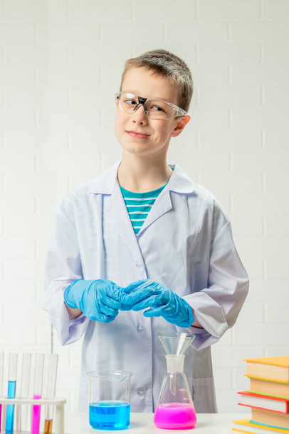 Een schooljongen bestudeert veelkleurige stoffen in reageerbuisjes, voert experimenten uit - een portret op een witte achtergrond. Concept voor de studie van het coronavirus in het laboratorium - Foto, afbeelding