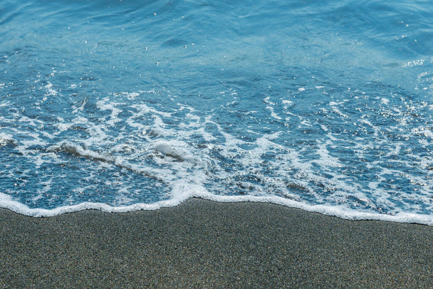 Белая пена волны на черном песке пляжа крупным планом - Фото, изображение