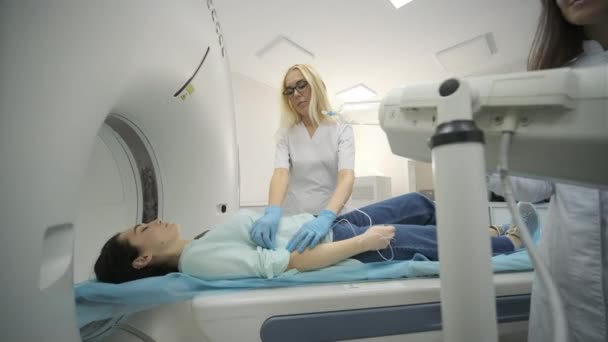 "CTまたはMRIスキャンを受けている女性患者とのコントラストを注入するために、 2人の放射線技師が静脈内カテーテルを挿入します。CTまたはMRIスキャンベッドに横たわっ患者 - 映像、動画