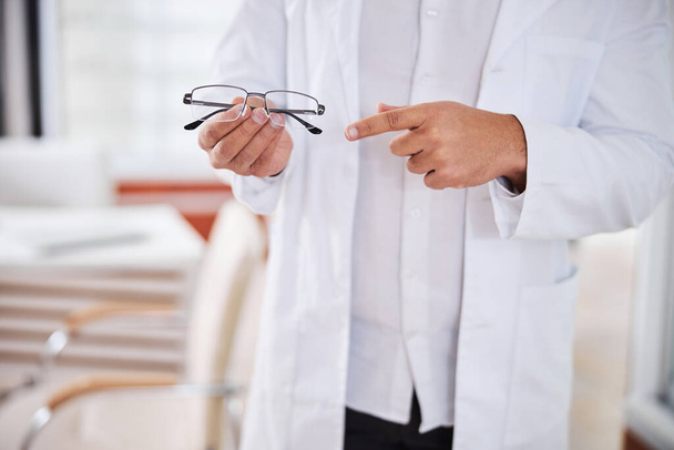 Оптометрист в лабораторном халате показывает рецептурные очки - Фото, изображение