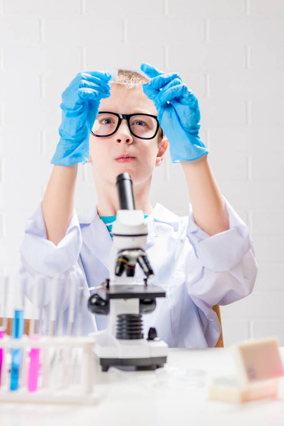 A schoolboy with a microscope examines chemicals in test tubes, conducts experiments - a portrait on a white background. Concept for the study of coronavirus in the laboratory - Foto, Bild