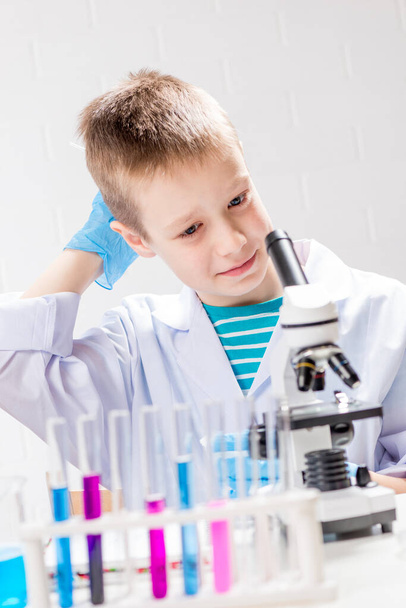 A schoolboy with a microscope examines chemicals in test tubes, conducts experiments - a portrait on a white background. Concept for the study of coronavirus in the laboratory - Photo, Image