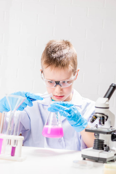 Uczeń z mikroskopem bada chemikalia w probówkach, przeprowadza eksperymenty - portret na białym tle. Koncepcja badania koronawirusu w laboratorium - Zdjęcie, obraz